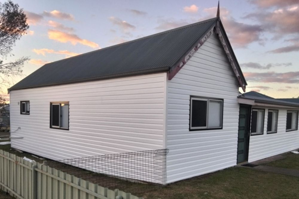 White weatherboard house with dark roof and windows at sunset, showing clean siding and modern trim-